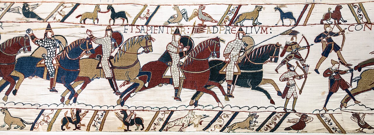 Mounted figures advance across the central strip beside archers on foot. Long shields, patterned clothing, horses, bows, and raised weapons distinguish bodies and actions. A line of lettering runs above them.