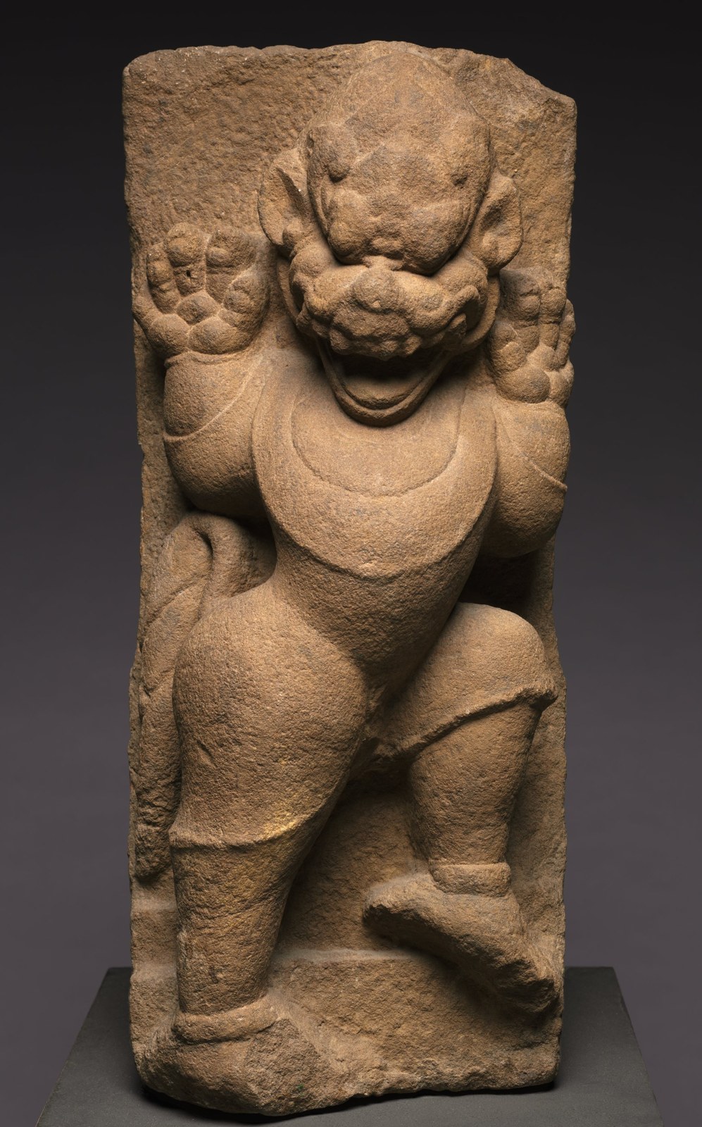 A sandstone lion-like figure rises with lifted forelimbs, prominent eyes, an open mouth, and a heavy chest ornament. Its surviving stone surface is worn and uneven.