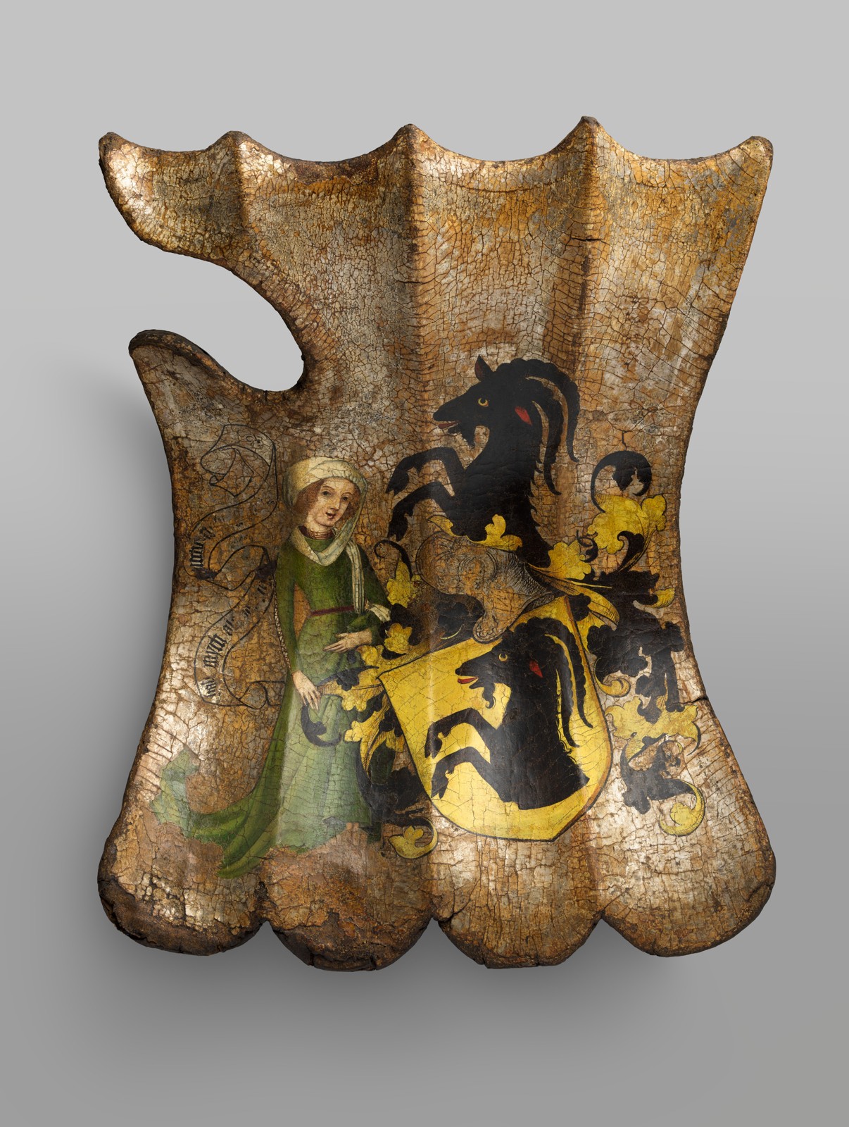 A scalloped tournament shield painted with a woman, a yellow armorial shield bearing a black animal head, and a helmet with a matching crest above it.
