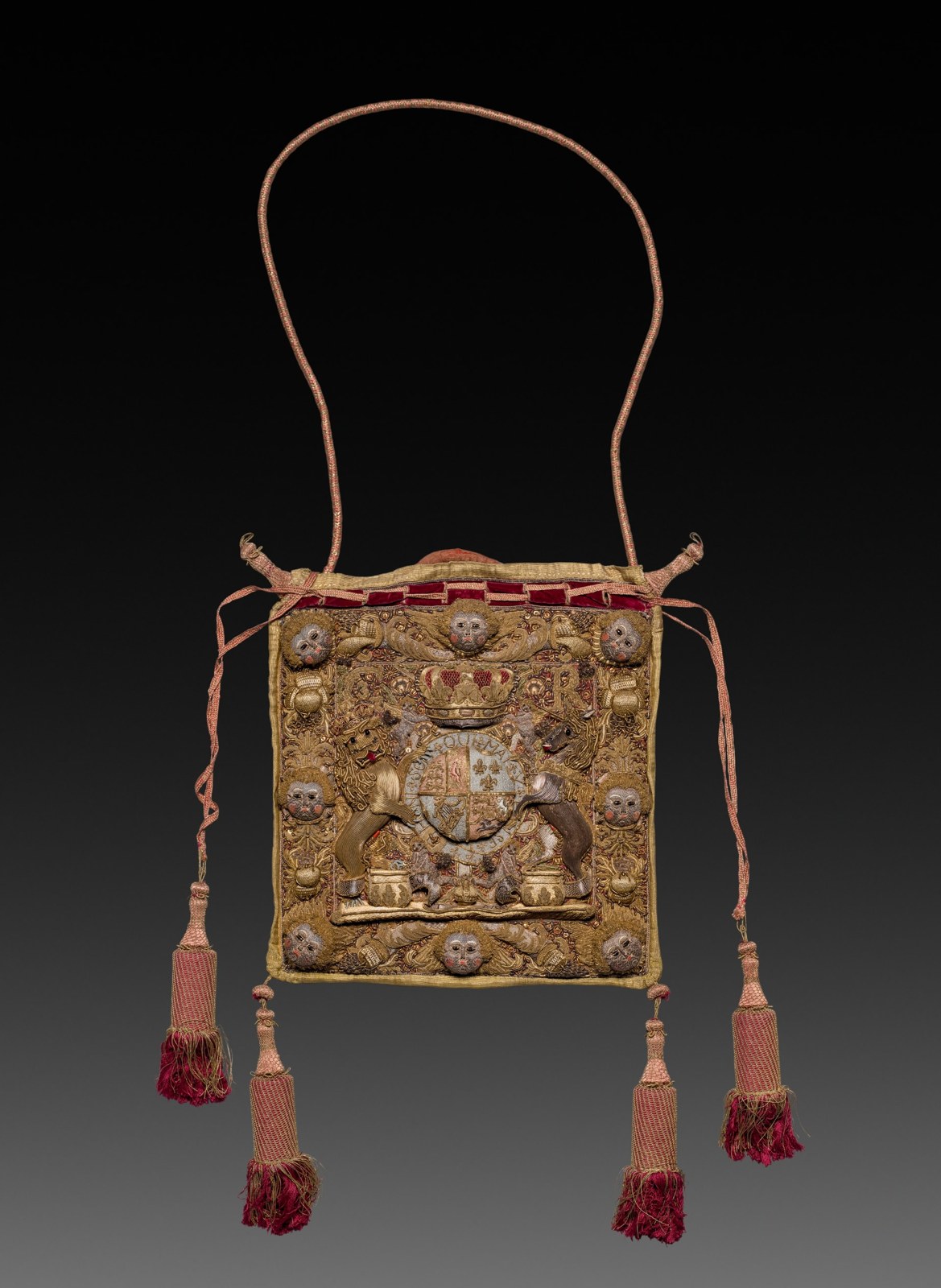 A small decorated purse hangs from cords and long tassels. Its front is densely worked with a crowned achievement, flanking animals, letters, and raised ornamental elements.