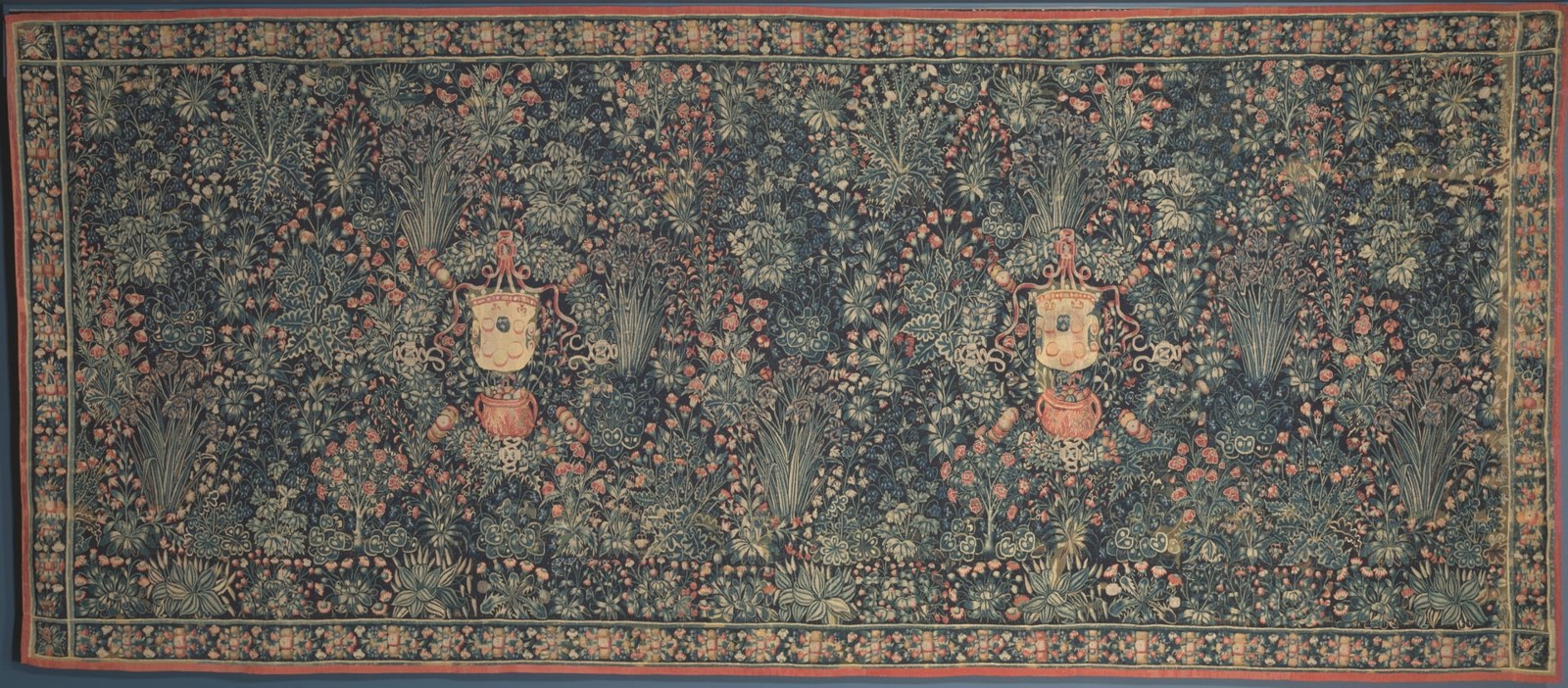 Two circular armorial displays interrupt a dense field of flowers. A narrow border encloses the horizontal textile, while repeated plant forms continue between the shields.