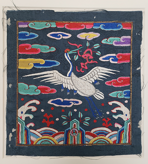 A white crane with spread wings appears amid colorful clouds and stylized rocks on a dark silk badge with frayed outer edges.